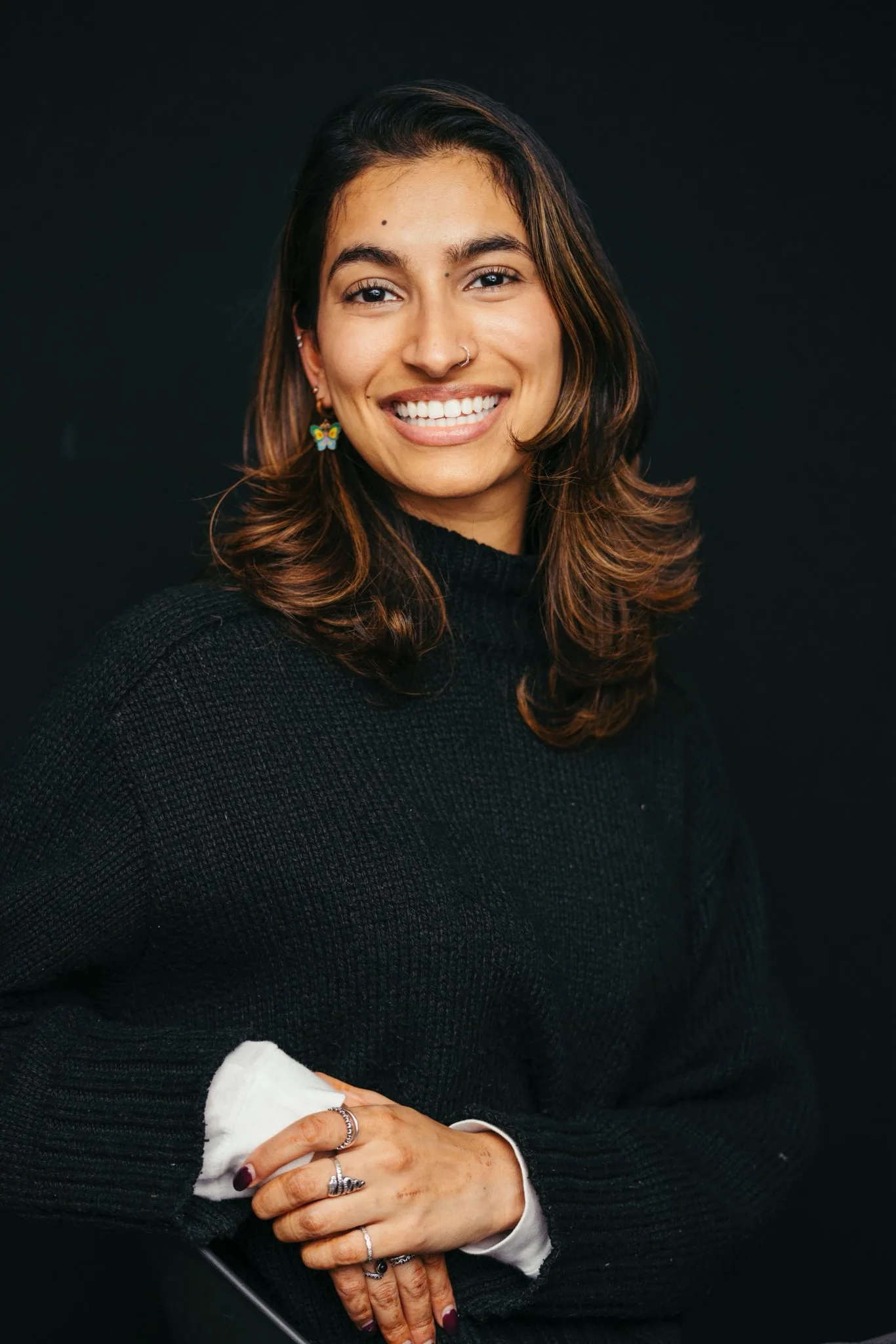 Dr Deesha, smiling in a black roll-neck against a dark studio backdrop